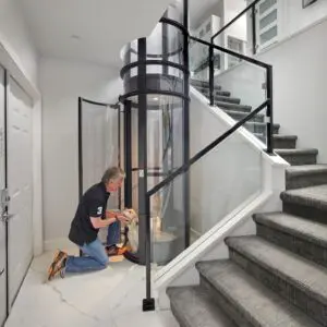 Man installing a glass elevator in a modern home staircase.