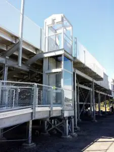Metal bleachers with an elevator and fenced walkway under clear sky.