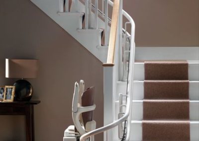 A white stair case with brown carpet and wooden handrail.