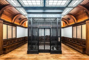 Elegant vintage glass elevator in a classic wooden-paneled room with a skylight ceiling.