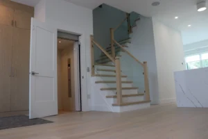 Modern staircase with glass railing and elevator beside it in a white interior.