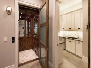 A vintage residential elevator with wooden interior next to a modern kitchen.